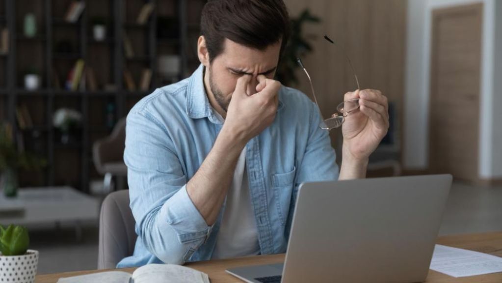 A man looking stressed or fatigued while working on a laptop.