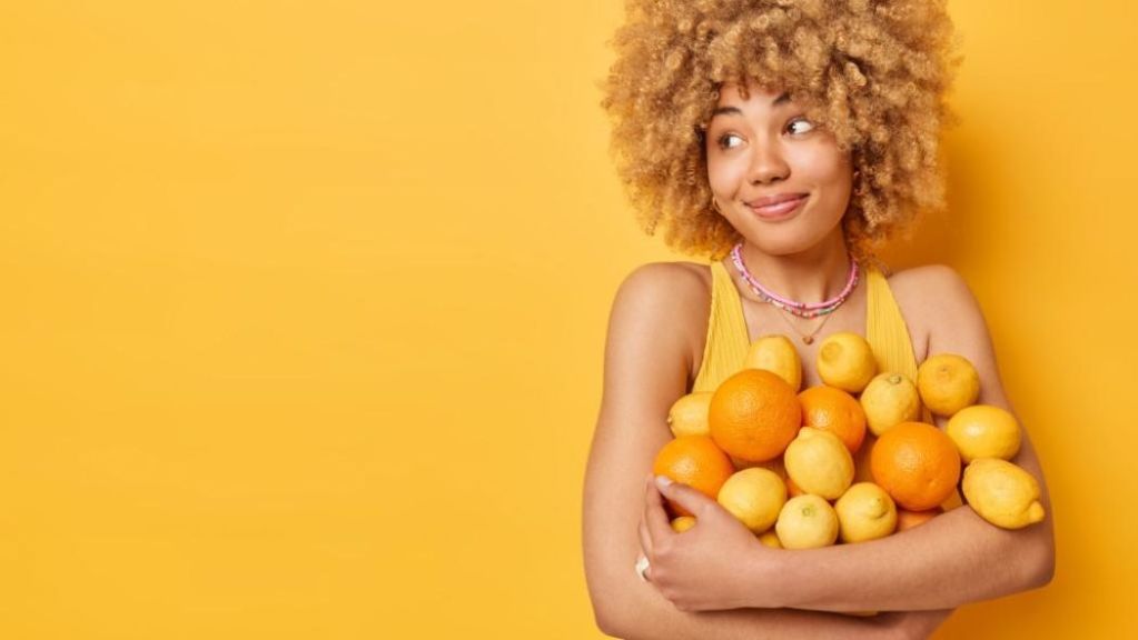 A person holding a bunch of citrus fruits against a yellow background.