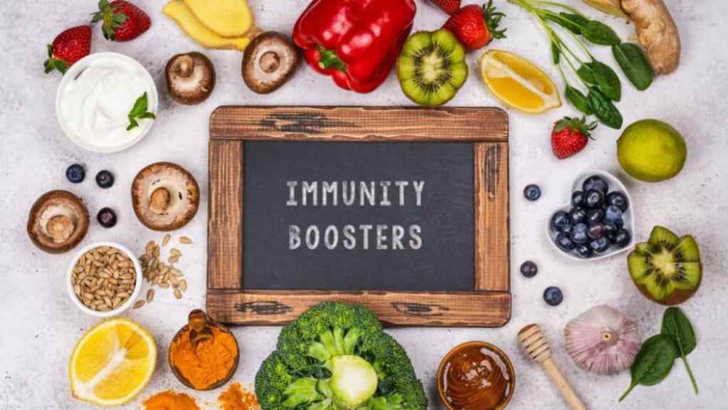 Various nutritious foods and a chalkboard with the words "immunity boosters" displayed on a light background.
