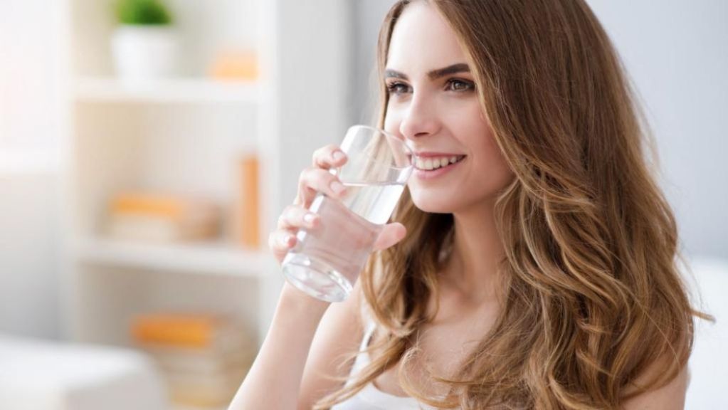 Woman smiling while drinking a glass of water indoors.