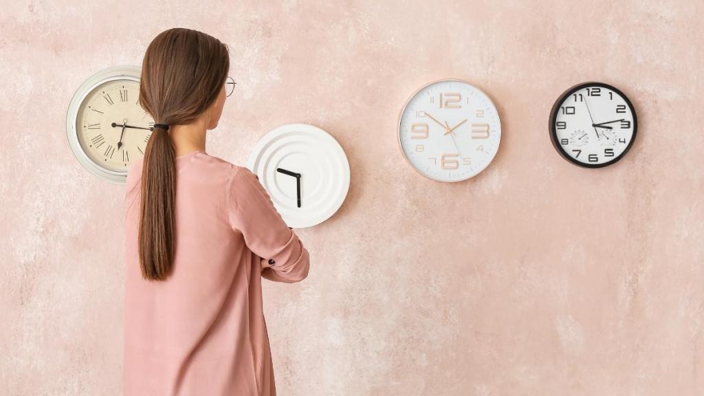 Woman looking at a wall with various clocks, displaying different times.
