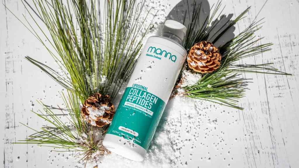 A bottle of liposomal collagen peptides lies on a white wooden surface, partially covered in snow, surrounded by pine needles and pinecones.