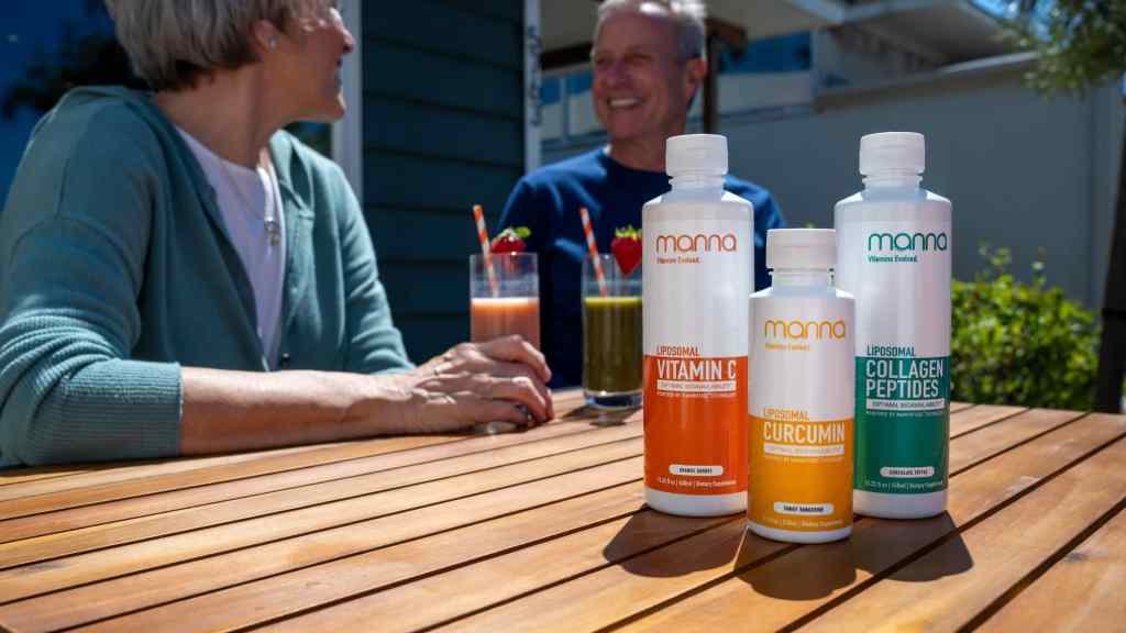 Two people chat at a table with vitamin supplements and colorful drinks, smiling in a sunny outdoor setting.