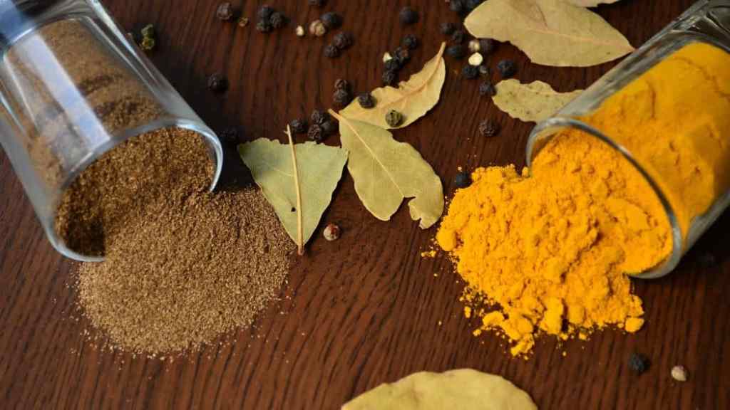 Spilled ground spices with bay leaves on a wooden surface.