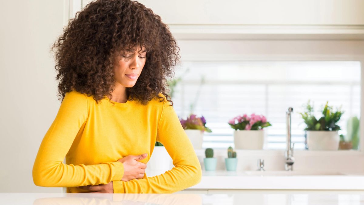 Woman in yellow sweater experiencing stomach pain or discomfort.