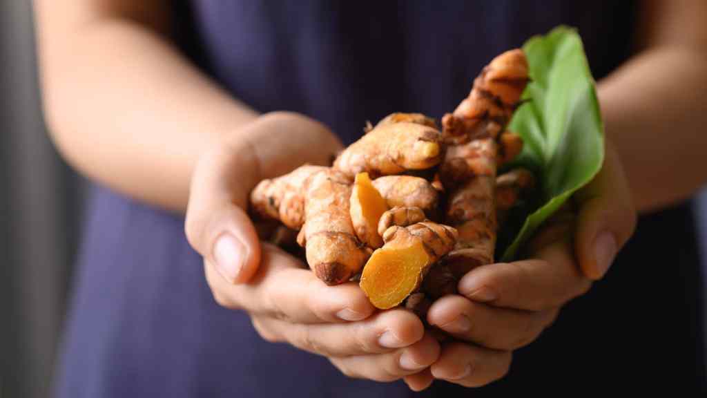 Hands holding several pieces of turmeric root with a green leaf.