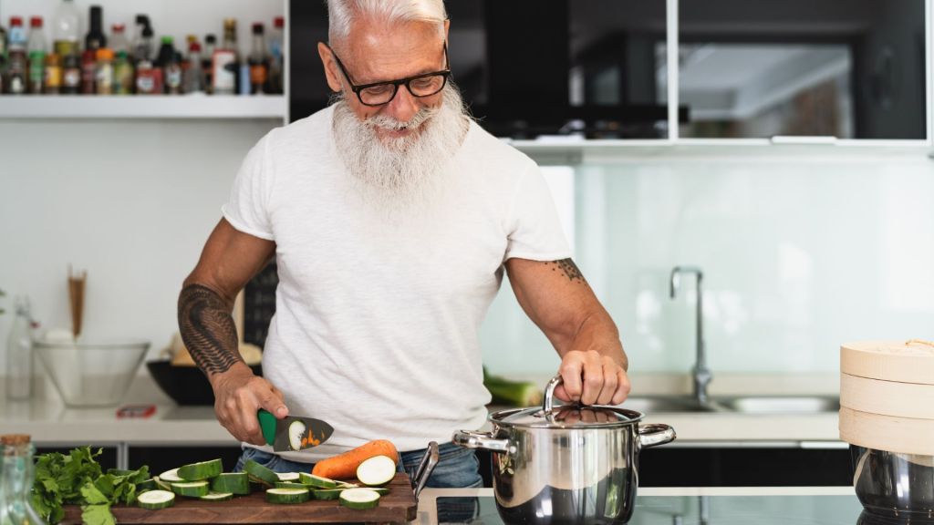 old man holding a pot cooking veggies