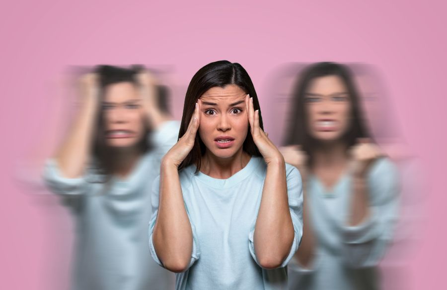 Woman looking stressed with hands on temples, showing motion blur of her head shaking, on pink background.