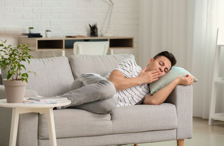 Young man sleeping peacefully on a gray couch in a bright, tidy living room.