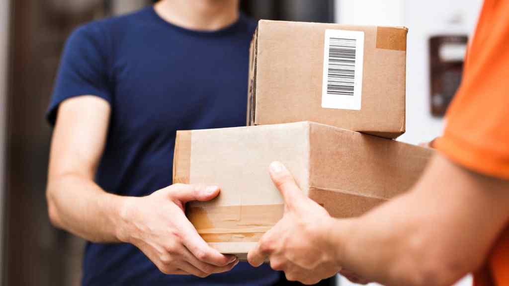 A person in a blue shirt receives two packages from another person in an orange shirt.