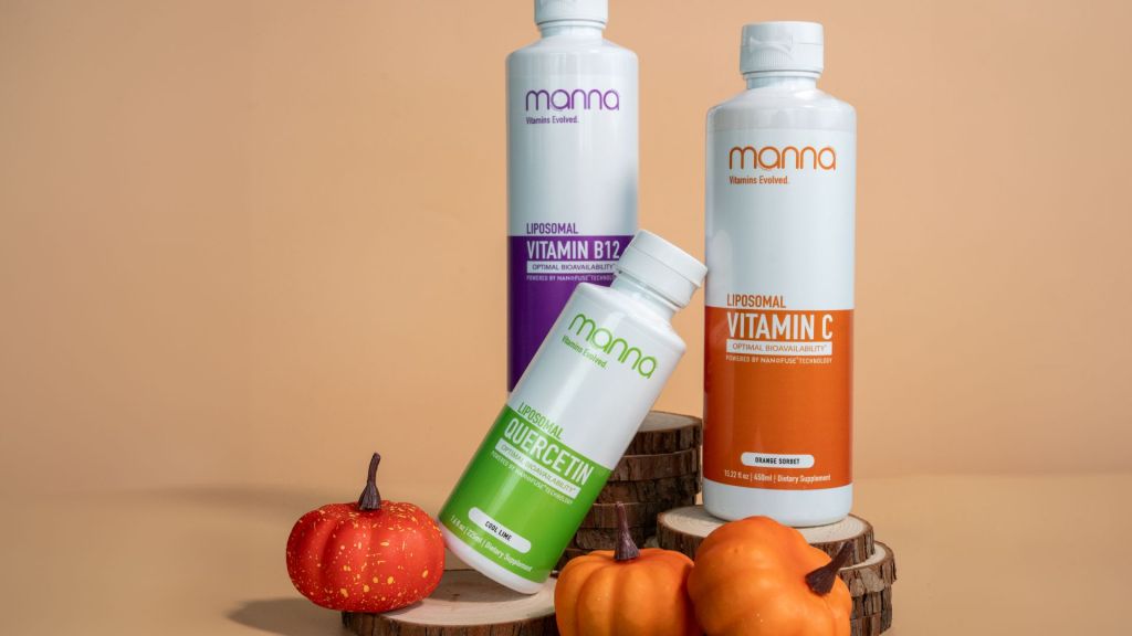 Three bottles of liposomal vitamins are displayed on wooden surfaces alongside small decorative pumpkins.