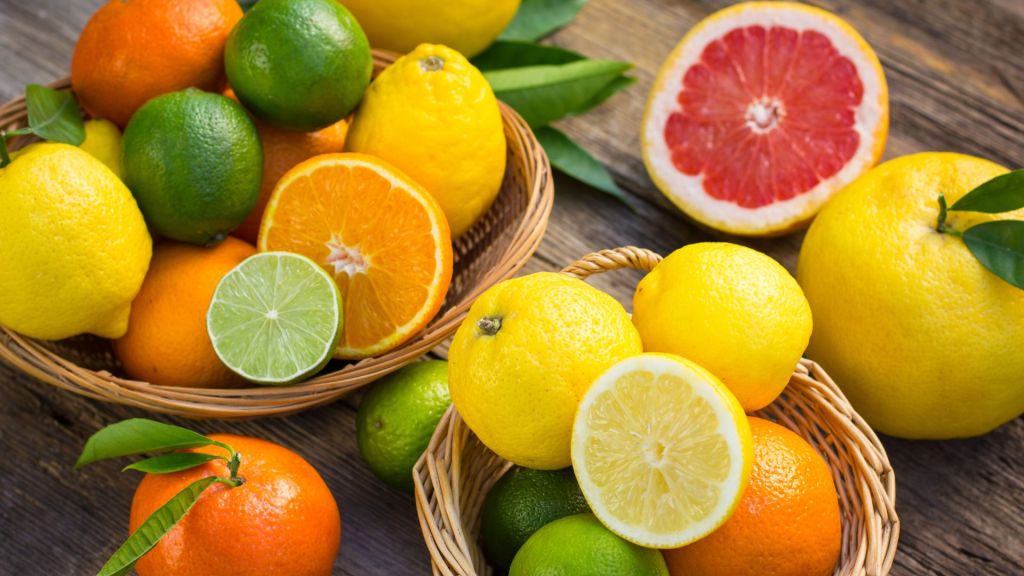 Baskets of assorted citrus fruits including lemons, oranges, limes, tangerines, and a halved grapefruit on a wooden surface.