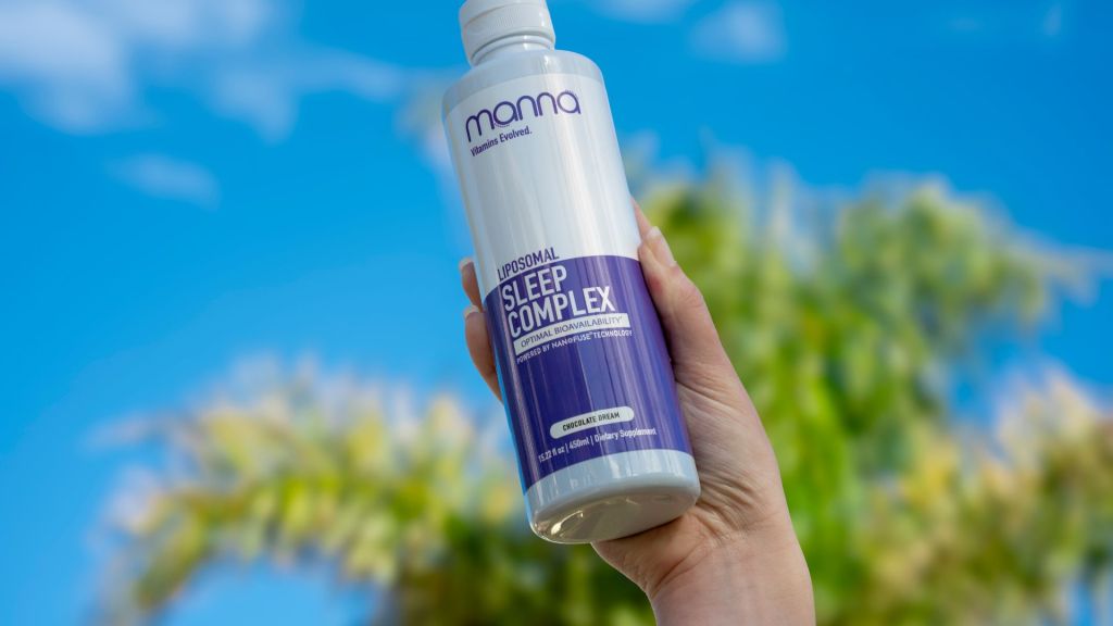 Hand holding a bottle of "Liposomal Sleep Complex" against a bright blue sky and leafy background.