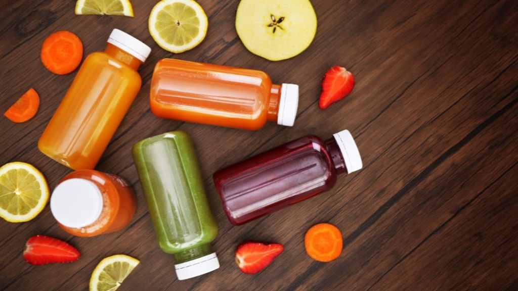 Assorted bottles of fresh juice with fruit slices on a wooden surface.