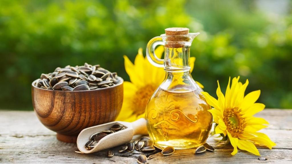 Sunflower seeds in a bowl, sunflower oil, and sunflowers resting on an outdoor wooden table.