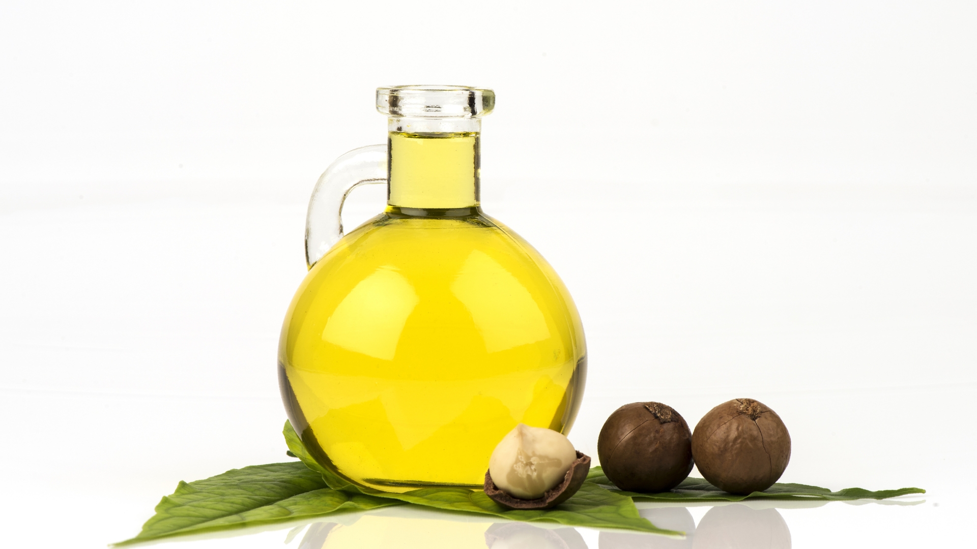 Olive oil in a glass jar resting on leaves with olives next to it.