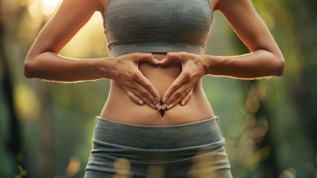 Person in athletic wear forms a heart shape with hands over their stomach outdoors.