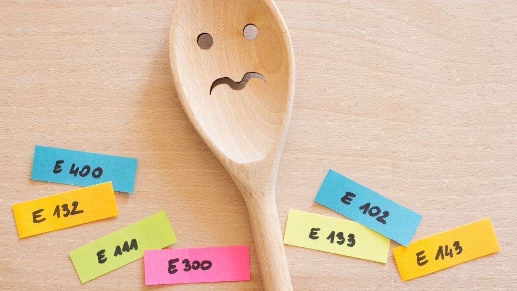 Wooden spoon with a frowning face surrounded by sticky notes with artificial ingredients written on them.
