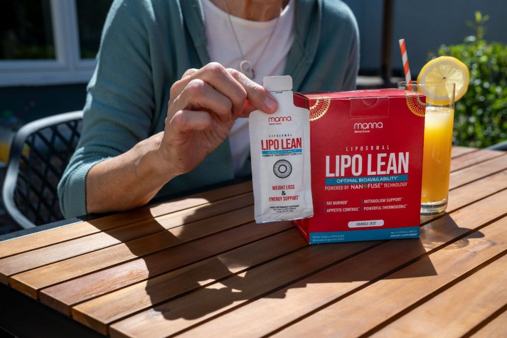 A person holding a packet of Lipo Lean supplement with a box and a glass of orange drink with a lemon slice on a table.
